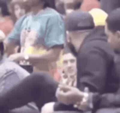 A Group Of People Are Sitting In A Stadium Watching A Game And One Of Them Is Using A Cell Phone . GIF