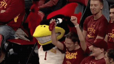 A Group Of People Are Sitting In A Stadium With A Mascot Wearing A Number 1 Shirt GIF
