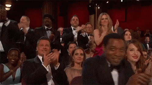 A Group Of People Are Sitting In A Theatre Clapping Their Hands . GIF