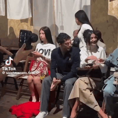 A Group Of People Are Sitting In Chairs Talking To Each Other While A Cameraman Takes A Picture Of Them . GIF