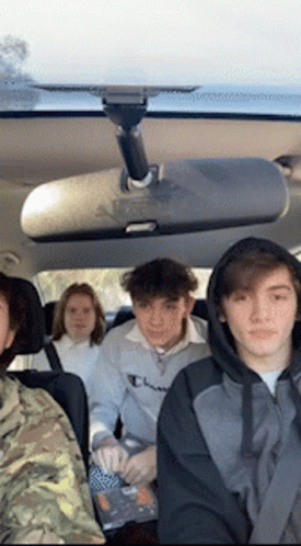A Group Of People Are Sitting In The Back Seat Of A Car Looking At The Rear View Mirror . GIF