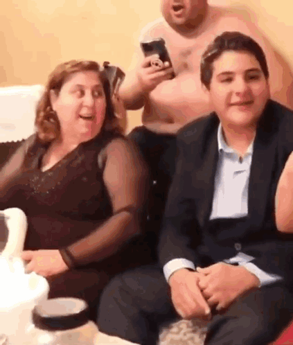 A Group Of People Are Sitting On A Couch And Laughing While A Man Holds A Cell Phone In His Hand . GIF
