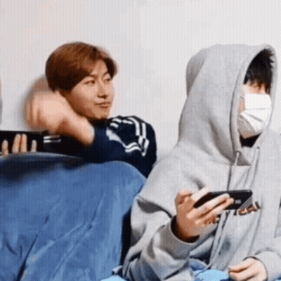 A Group Of People Are Sitting On A Couch And One Of Them Is Wearing A Mask While Holding A Cell Phone . GIF
