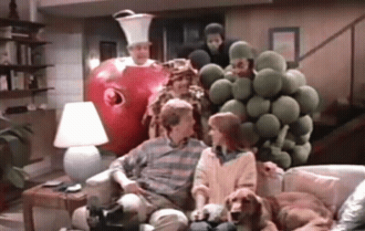 A Group Of People Are Sitting On A Couch In A Living Room With A Giant Apple Behind Them . GIF