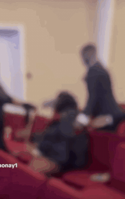 A Group Of People Are Sitting On Red Couches In A Room . GIF