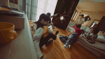 A Group Of People Are Sitting On The Floor In A Living Room And One Of Them Has The Word Adidas On His Back GIF