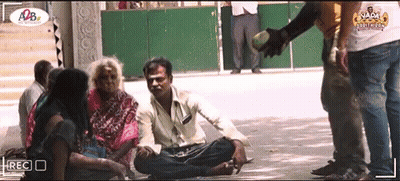A Group Of People Are Sitting On The Ground And A Man Is Giving A Bottle Of Water GIF