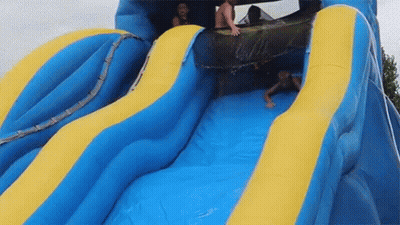 A Group Of People Are Sliding Down A Blue And Yellow Inflatable Water Slide . GIF