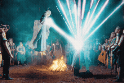 A Group Of People Are Standing Around A Fire With A Blue Light Coming Out Of The Sky GIF