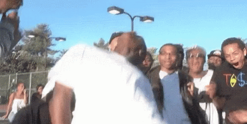 A Group Of People Are Standing Around A Man In A White Shirt With A Dollar Sign On The Front . GIF