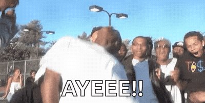 A Group Of People Are Standing Around A Man In A White Shirt With The Word Ayeeee Written On It . GIF