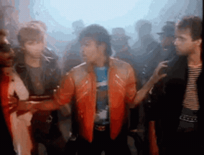 A Group Of People Are Standing Around A Man In An Orange Jacket . GIF
