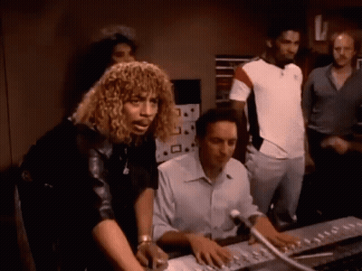 A Group Of People Are Standing Around A Man Sitting At A Desk GIF