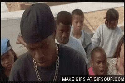 A Group Of People Are Standing Around A Man Wearing A Chain Around His Neck GIF
