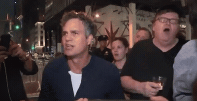 A Group Of People Are Standing Around A Man Who Is Holding A Glass Of Beer . GIF