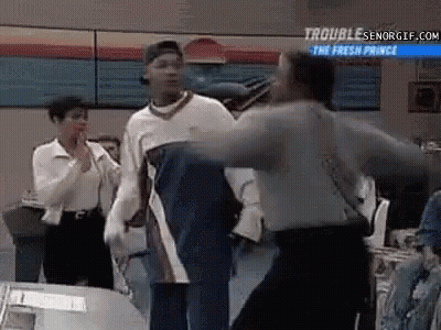 A Group Of People Are Standing Around A Table And A Man Is Standing In The Middle Of The Room . GIF