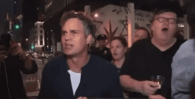 A Group Of People Are Standing Around A Table And One Of Them Is Holding A Glass Of Whiskey GIF