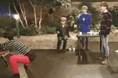 A Group Of People Are Standing Around A Table In A Room With Trees In The Background . GIF