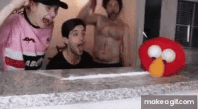 A Group Of People Are Standing Around A Table With A Stuffed Elmo . GIF