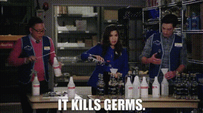 A Group Of People Are Standing Around A Table With Bottles Of Cleaning Supplies And The Words `` It Kills Germs '' . GIF