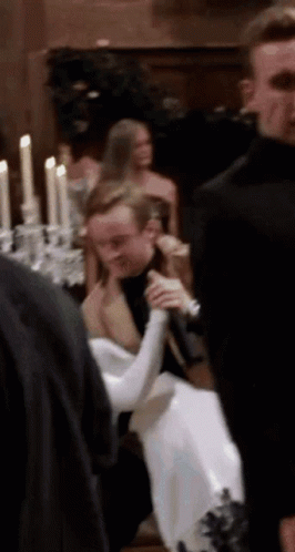 A Group Of People Are Standing Around A Table With Candles And A Man Holding A Microphone . GIF
