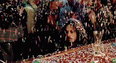 A Group Of People Are Standing Around A Table With Confetti Falling On Them . GIF