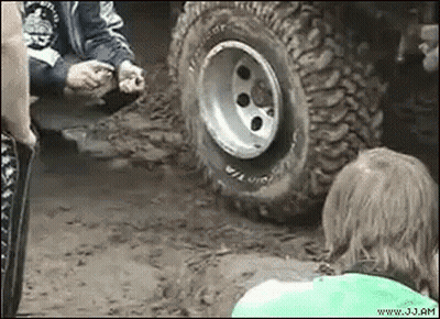 A Group Of People Are Standing Around A Tire Of A Jeep . GIF