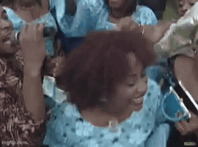 A Group Of People Are Standing Around A Woman In A Blue Dress Holding A Microphone . GIF