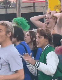 A Group Of People Are Standing In A Crowd And One Of Them Is Wearing A Green Jacket GIF