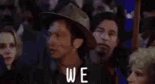 A Group Of People Are Standing In A Crowd With The Words `` Again '' Written On The Bottom . GIF