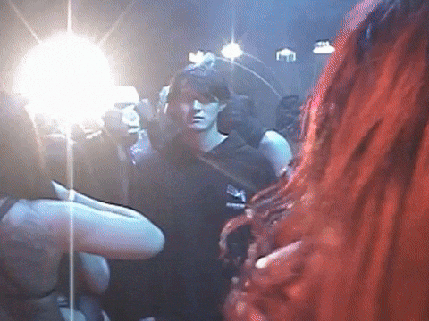 A Group Of People Are Standing In A Dark Room And One Of Them Is Wearing A Black Shirt That Says ' A ' GIF