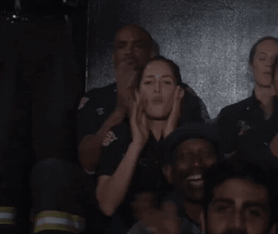 A Group Of People Are Standing In A Dark Room And One Of Them Is Wearing A Black Shirt With The Letter T On It GIF