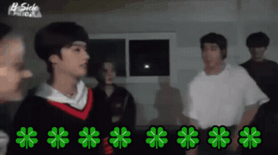 A Group Of People Are Standing In A Dark Room With Green Clovers On The Floor GIF