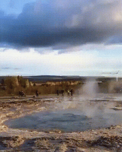 A Group Of People Are Standing In A Field Near A Waterfall GIF
