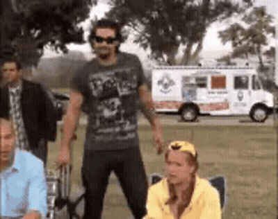 A Group Of People Are Standing In A Field With A White Truck In The Background . GIF