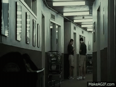 A Group Of People Are Standing In A Hallway Talking To Each Other . GIF