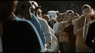 A Group Of People Are Standing In A Line Playing Musical Instruments . GIF