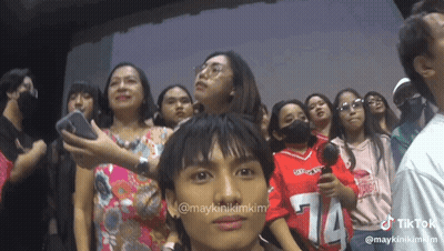 A Group Of People Are Standing In A Room And One Of Them Is Wearing A Red Shirt With The Number 14 On It GIF