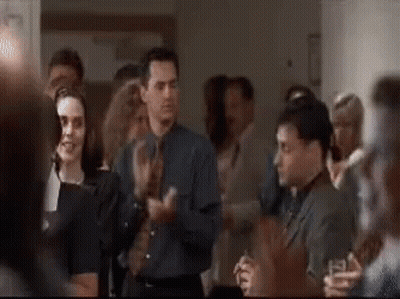 A Group Of People Are Standing In A Room Applauding Each Other . GIF