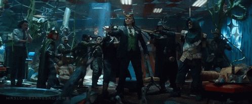 A Group Of People Are Standing In A Room With A Man In A Suit And Horns . GIF