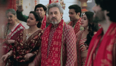 A Group Of People Are Standing In A Room With A Man Wearing A Red Scarf Around His Neck . GIF