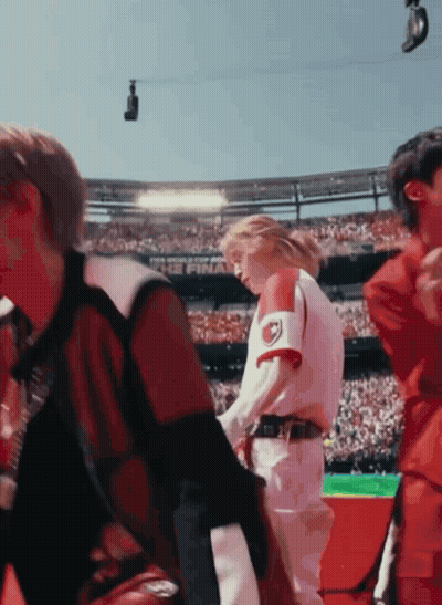 A Group Of People Are Standing In A Stadium And One Of Them Is Wearing A Red And White Jersey With The Letter R On It GIF
