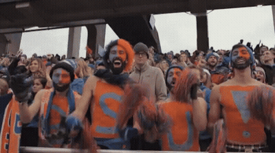 A Group Of People Are Standing In A Stadium Wearing Orange And Blue Shirts With The Letter S Painted On Them . GIF