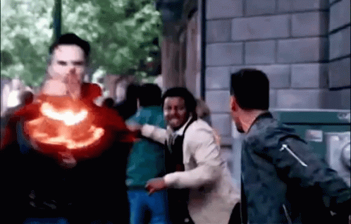 A Group Of People Are Standing In Front Of A Building While A Man Is Holding A Red Object In His Hand . GIF