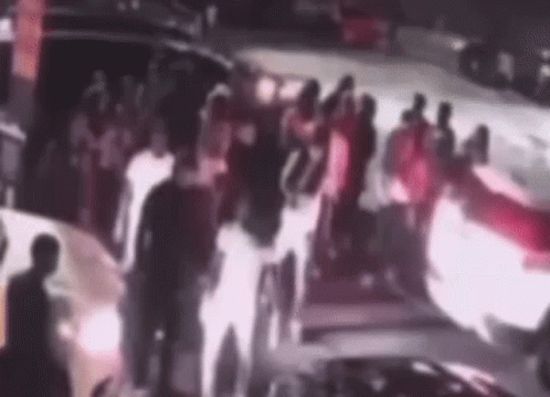 A Group Of People Are Standing In Front Of A Car With A Fire Coming Out Of It . GIF