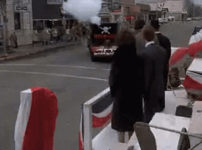 A Group Of People Are Standing In Front Of A Car With A Flag On The Back . GIF