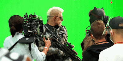 A Group Of People Are Standing In Front Of A Green Screen With A Camera That Says Lx On It GIF