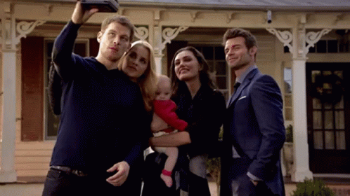 A Group Of People Are Standing In Front Of A House Taking A Selfie With A Baby . GIF