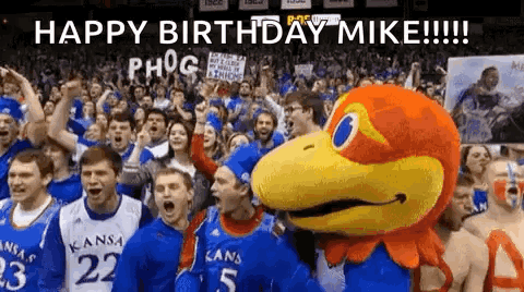 A Group Of People Are Standing In Front Of A Mascot And A Sign That Says `` Happy Birthday Mike '' . GIF
