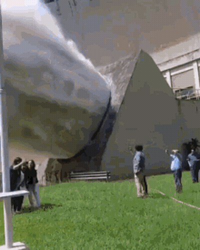 A Group Of People Are Standing In Front Of A Pyramid In A Park . GIF